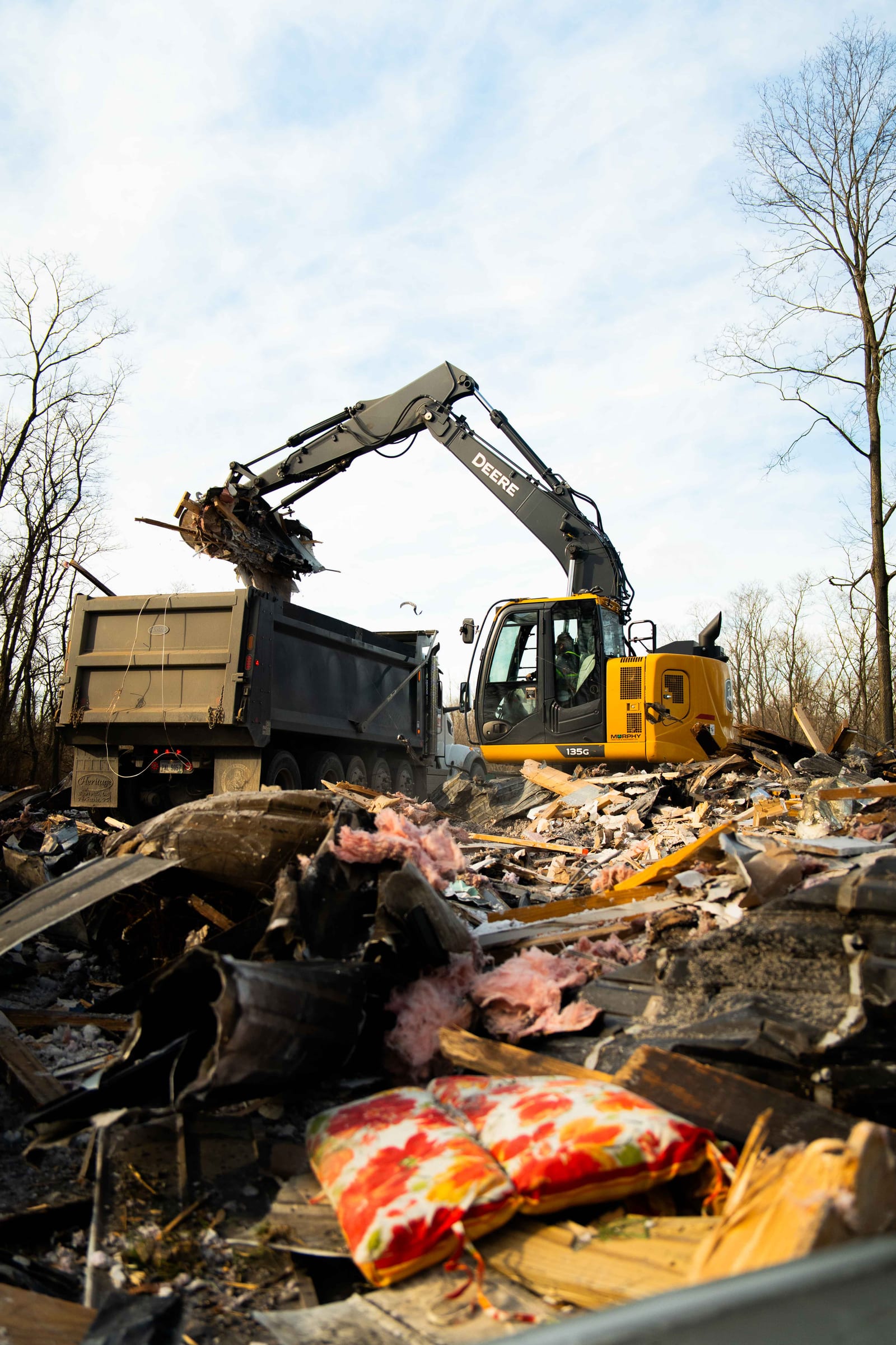 An excavator loading household debris into a dump truck during a clear-out